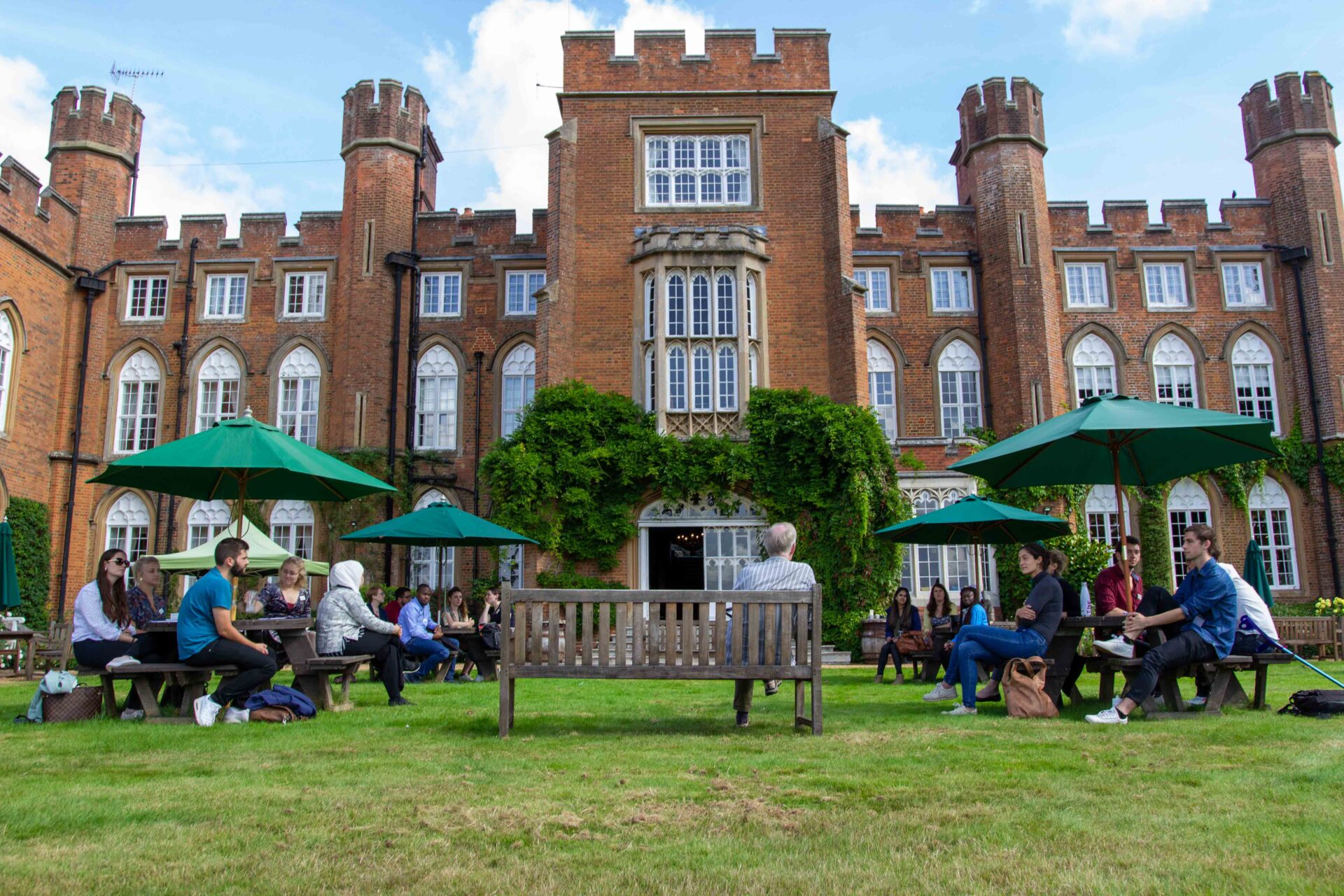 People sitting on picnic benches on the lawn outside Cumberland Lodge