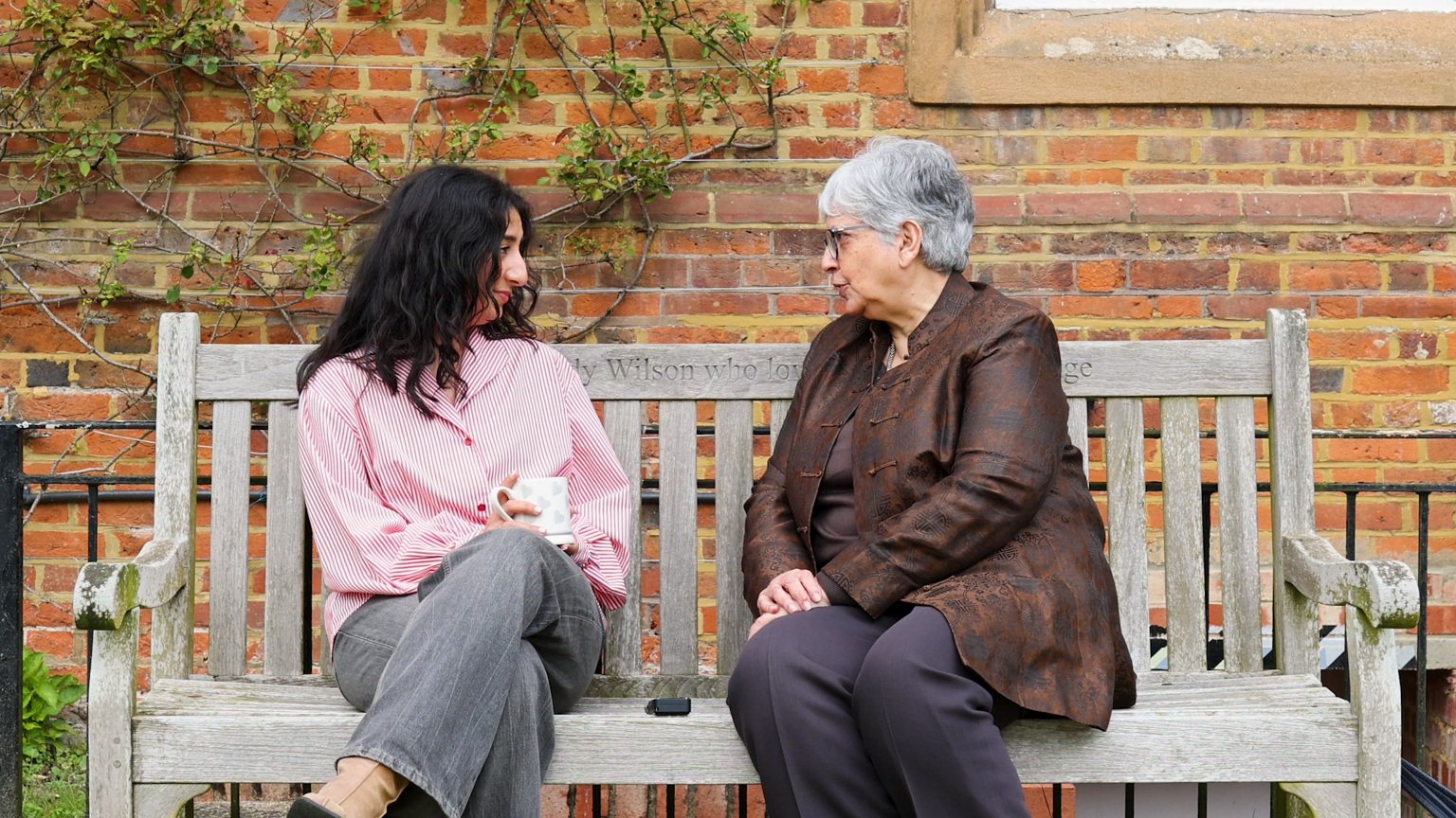 An intergenerational conversation between Munny Purba and Baroness Usha Prashar, sat on a bench outside Cumberland Lodge